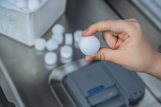 Woman's hand putting water softener salt tablets into dishwasher to prevent limescale