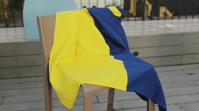 The flag of Ukraine is hanging on a chair on a wooden terrace, a yellow and blue flag. 