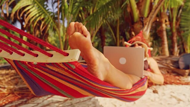 Bare Foot Resting On Colorful Hammock While Person Works On Laptop Under Palm Trees Creating Relaxed Remote Work Lifestyle In Tropical Nature