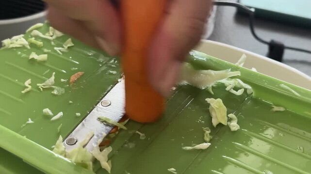 Professional chef person making organic fresh co salad cutting carrot on a metal mandolin cutter, grater, slow motion