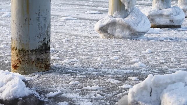 Frozen sea slush ice surrounding rusted metal pillars in cold winter morning light