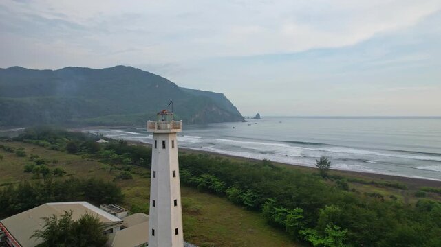 Aerial drone footage of the Puger beach lighthouse in Jalan Lintas Selatan, nearby the coast, in Lumajang regency, Java island, Indonesia, with cliffs and the sea behind, at cloudy sunset time