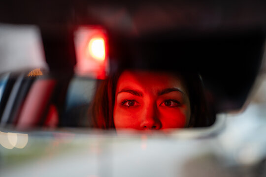 Woman driving car at night seeing red light in rearview mirror