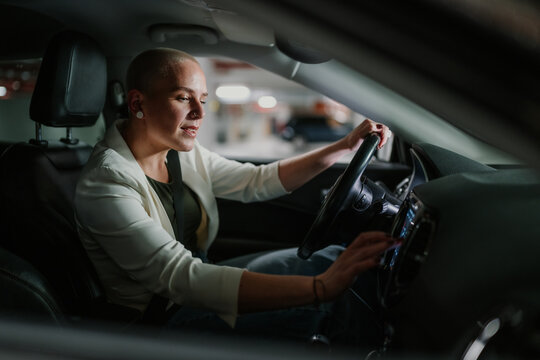 Confident bald woman driving car and operating modern infotainment system in parking garage at night