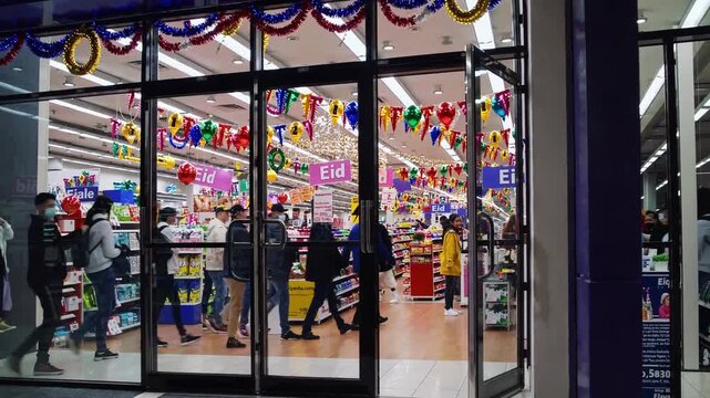 Shopfront With Festive Lights And Shoppers. Bright Supermarket Doorway Adorned With Holiday Decorations And Customers. Lively Retail Setting With Colorful Decorations And Busy Shoppers Entering