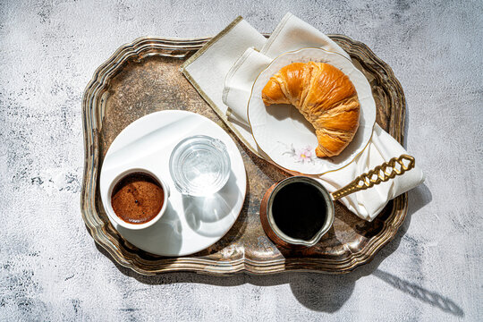 A cup of coffee, fresh croissant,coffee pot on a table with sunlight. Table set for breackfast. Flat lay.