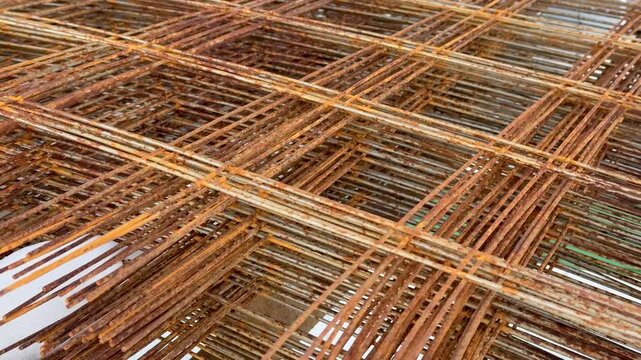 Rusty rebar rods stacked outdoors, closeup showing corroded ribbed steel, overlapping mesh pattern with warm orange brown patina.