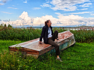 Fototapeta premium Middle aged woman relaxes on a weathered boat in a serene natural landscape during a clear day