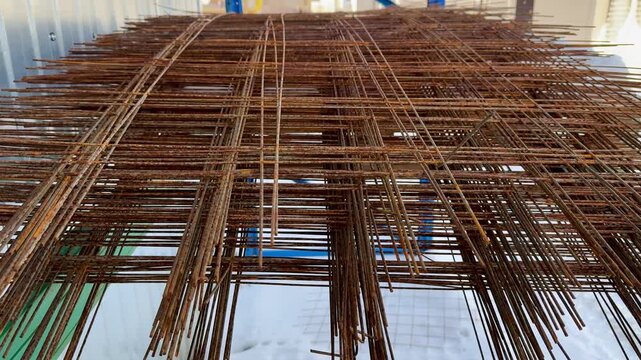 Rusty rebar rods stacked outdoors, closeup showing corroded ribbed steel, overlapping mesh pattern with warm orange brown patina.