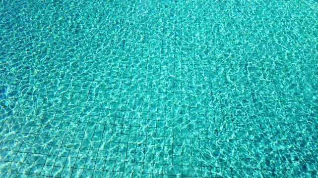 Tiles on the bottom of a pool with water rippling in slow motion on a sunny day as a background or graphic pattern, empty space for text.