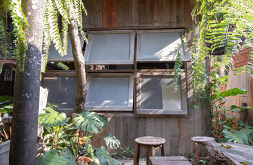 Tucked away in a lush corner, this rustic sanctuary features a weathered wooden facade with awning windows that invite a gentle breeze. Dappled sunlight filters through hanging ferns and broad monster