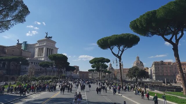 Many people walking on street Via dei Fori Imperiali on sunny day in Rome with view of Alter of Fatherland in background, slow motion aerial shot