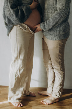 Stylish pregnant couple hugging baby bump close up. Fertility, health care and expecting new life concept. Happy Mothers day. Family in cozy sweaters and jeans holding pregnant belly