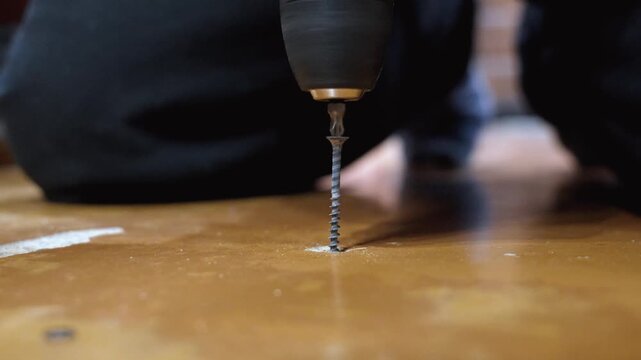 Close-up of professional worker working with cordless drill screwing long screw into wooden board during assembly or repair, showing the precision and power of modern tools