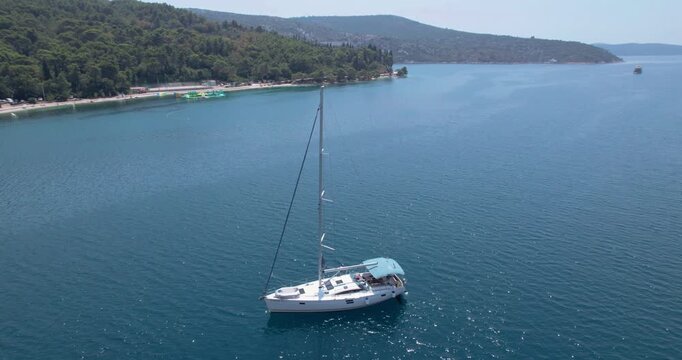 Aerial Yacht Anchored Near Pier, Calm Turquoise Water And Forested Shoreline, Lone Vessel Bobbing Gently With Sunlight Glint On Hull, Slow Cinematic Drone Reveal