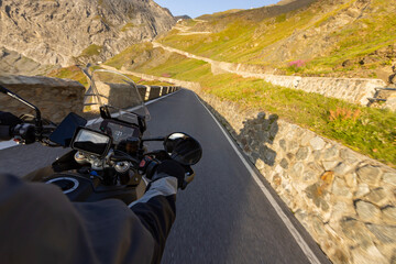 Motorcycle rider riding in Italian Alps during sunrise , handlebar view , dramatic sky . Travel and freedom, outdoor activities