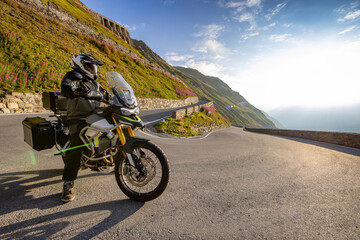 Motorcycle rider posing in Italian Alps during sunrise, dramatic sky. Travel and freedom, outdoor activities