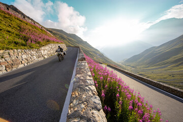 Motorcycle rider riding in Italian Alps during sunrise, dramatic sky. Travel and freedom, outdoor activities
