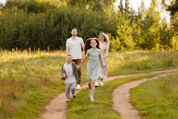 Fototapeta premium Family Running Along Dirt Path Under Golden Sunlight, Parents Smiling While Children Lead The Way Through Tall Grass And Wildflowers, Candid Motion Capturing Playful Energy And Authentic