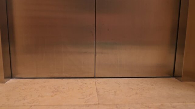 autonomous robot vacuum cleaner stops at the open elevator threshold on the tiled floor and moves inside, the doors closing, hinting at intelligent home cleaning inside a modern residential building.