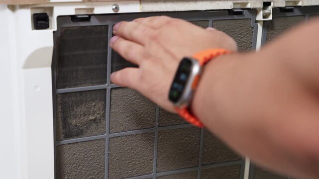 Close up of vacuum cleaner nozzle removing dust from a square air filter grid, home maintenance cleaning of ventilation screen with tiled wall background and shallow depth of field, visible lint