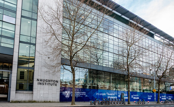 Naughton Institute, Trinity College Dublin on Pearse Street, Ireland. A glass building with bare trees and a row of rental bicycles in front.