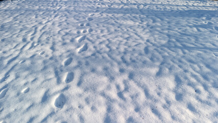 Footprints visible on a white snow-covered surface create a textured pattern. The serene winter scene evokes a sense of quiet nature, perfect for travel and outdoor themes. © daily_creativity