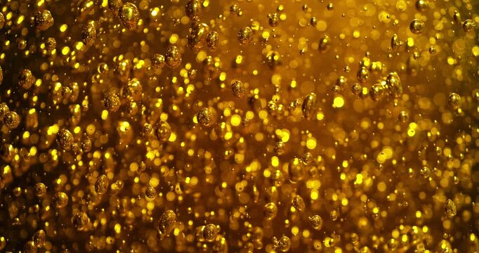 Extreme super slow motion of golden liquid, oil with rising bubbles and sparkling highlights, creating an abstract macro background with dynamic motion and rich amber tones.