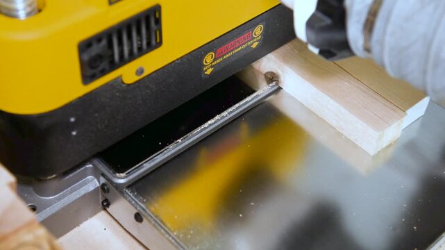 A wood plate passing through the thickness planer machine in a carpentry workshop. Woodworking process, furniture preparation, handmade craftsmanship, carpentry studio.