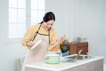 キッチンでパソコンを見ながら料理をする主婦