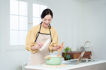 キッチンでパソコンを見ながら料理をする主婦