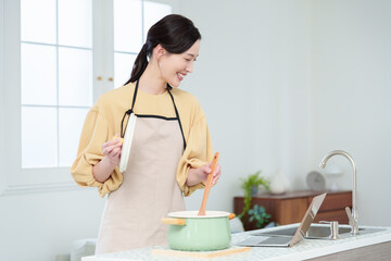 キッチンでパソコンを見ながら料理をする主婦