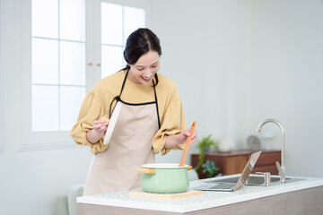 キッチンでパソコンを見ながら料理をする主婦