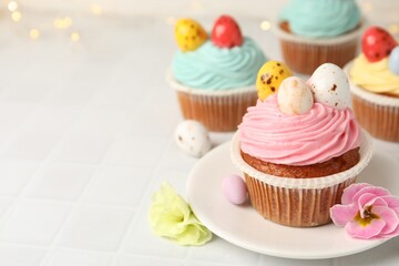Tasty cupcakes with Easter decor on white tiled table, closeup. Space for text