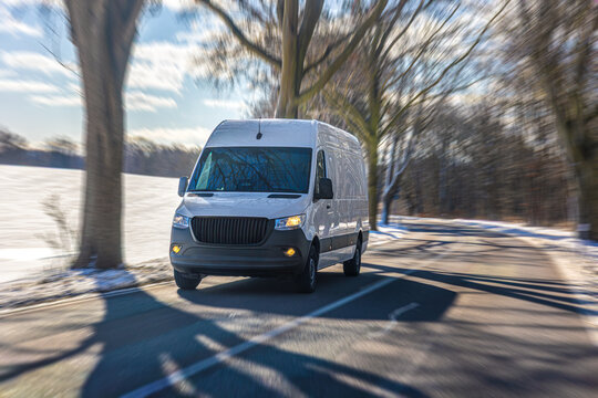 White delivery van driving on winter road near snowy field. Commercial transport concept.