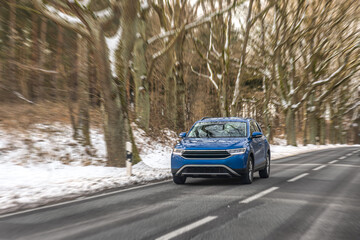 Fototapeta premium Blue crossover driving on snowy forest road. Winter car travel.
