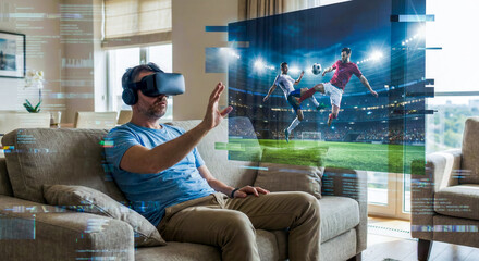 Concept of a man sitting on a sofa wearing VR goggles and holding controllers, experiencing an immersive 3D holographic soccer match broadcast in a modern living room