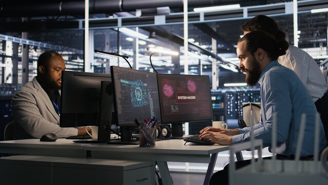 Anxious technicians in data center reacting to system lockdown caused by ransomware alert. IT professionals under pressure evaluating security breaches and scrambling to contain damage, camera A