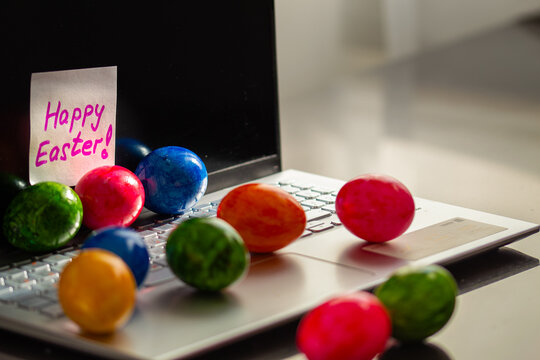 Colorful Easter eggs on the laptop, computer, sticky note saying Happy Easter!, grey background; technology and tradition