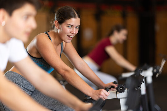 European woman on an intense cycling workout in the gym. Woman in top and leggings actively pedaling on an exercise bike