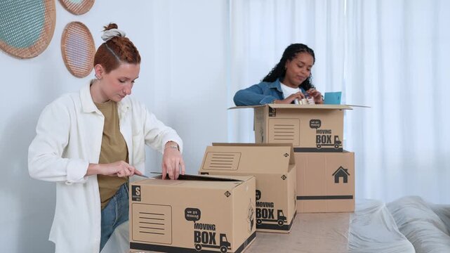 Lesbian couple packing cardboard moving boxes together in new apartment