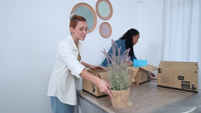 Diverse female couple unpacking belongings in new home