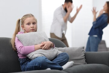Obraz premium Alimony. Sad little girl with pillow sitting on sofa while her parents arguing at home, selective focus