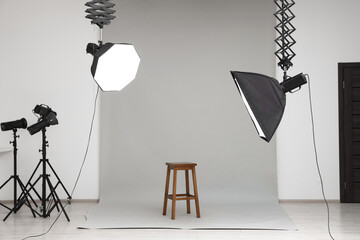 Professional lighting equipment hanging from ceiling and chair in photo studio