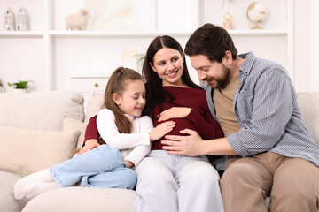 Pregnant woman, her husband and daughter on sofa at home
