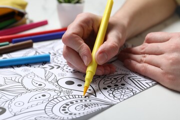 Woman coloring antistress picture with felt tip pen at white table, closeup
