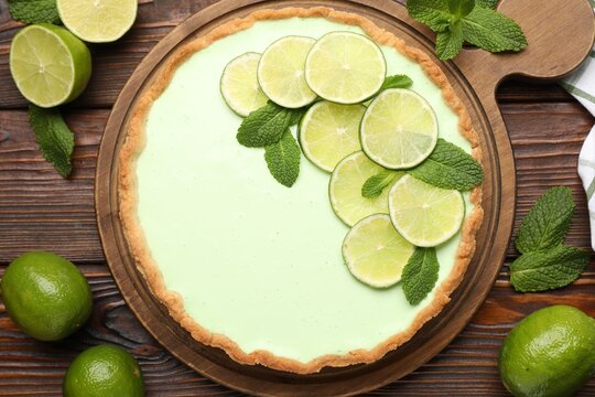 Tasty lime pie with fruit slices and mint leaves on wooden table, flat lay