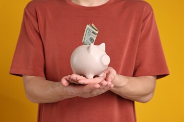 Man with piggy bank and banknote on orange background, closeup