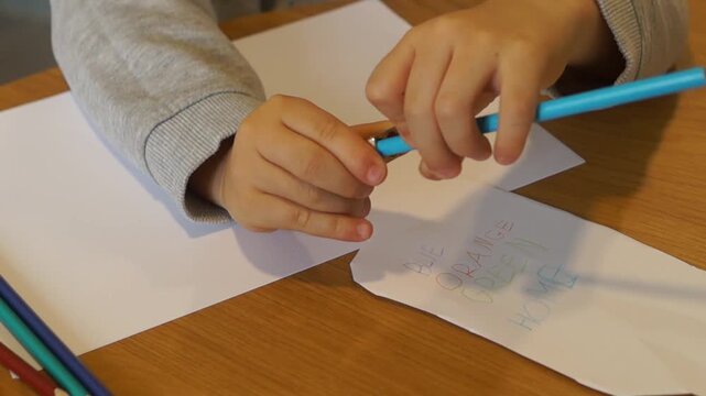 Close-up view of a left-handed boy's hands as he turns a blue pencil inside a metal sharpener over a craft project.