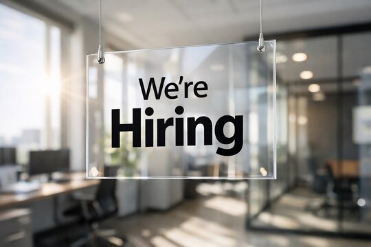 Glass sign with 'we're hiring' in modern office background with blurred desks and windows